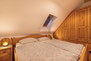 Relax in a warm and inviting bedroom with a large bed and patterned bedding, wooden cabinetry, and a bedside table with a lamp.
