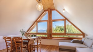 A dining area with a wooden table and chairs, a sofa, and large windows offering a view of greenery and a distant landscape. - Vineyard cottage Škatlar 3 (Novo Mesto)
