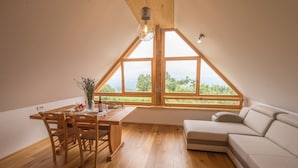 A room with a wooden dining table, chairs, a sofa, and large windows offering a view of greenery. - Vineyard cottage Škatlar 3 (Novo Mesto)