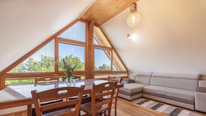 A dining area with a wooden table and chairs, a sofa, and large windows with a view of greenery. - Vineyard cottage Škatlar 3 (Novo Mesto)