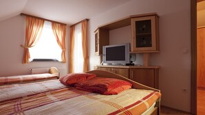 A bedroom with two beds, a television on a wooden cabinet, and a window with curtains. - Tourist Farm Skrbina (Smarjeske Toplice)
