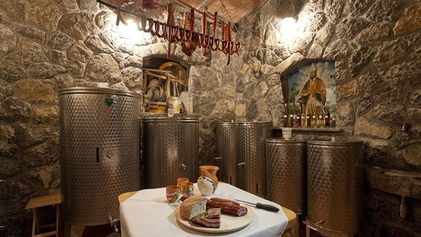A rustic cellar with stone walls, wooden barrels, and a table with food and drinks. - Tourist Farm Skrbina (Smarjeske Toplice)