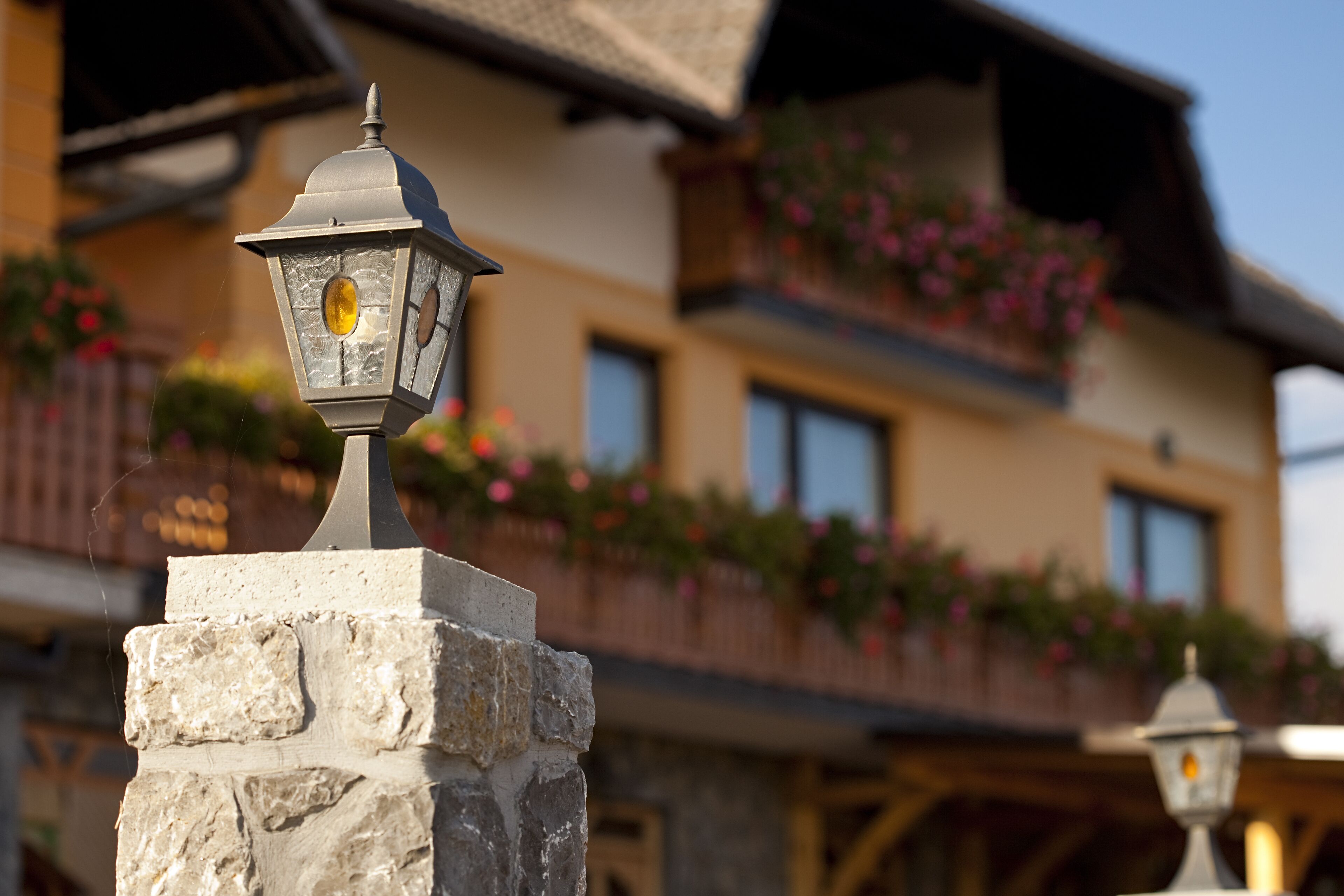 A stone lantern on a balcony railing, a wooden balcony with flower boxes, and a building facade with windows.