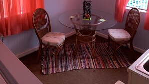 A dining area with a glass table, wicker chairs, a colorful rug, and red curtains. - Beach Side Studio #5 - Pet Friendly, WiFi, Off-Street Parking, Large Smart TV (Norfolk)