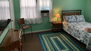 A room with a bed, a chair, a desk, a lamp, and a window with curtains. - Beach Side Studio #5 - Pet Friendly, WiFi, Off-Street Parking, Large Smart TV (Norfolk)