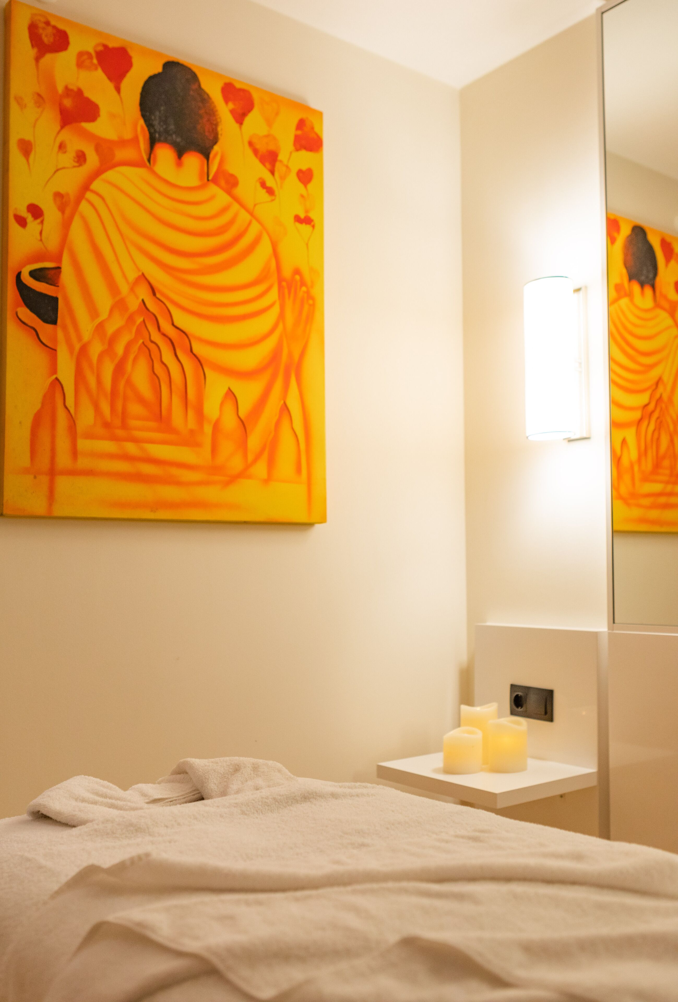 A hotel room with a bed, a bedside table with candles, and a large painting on the wall.