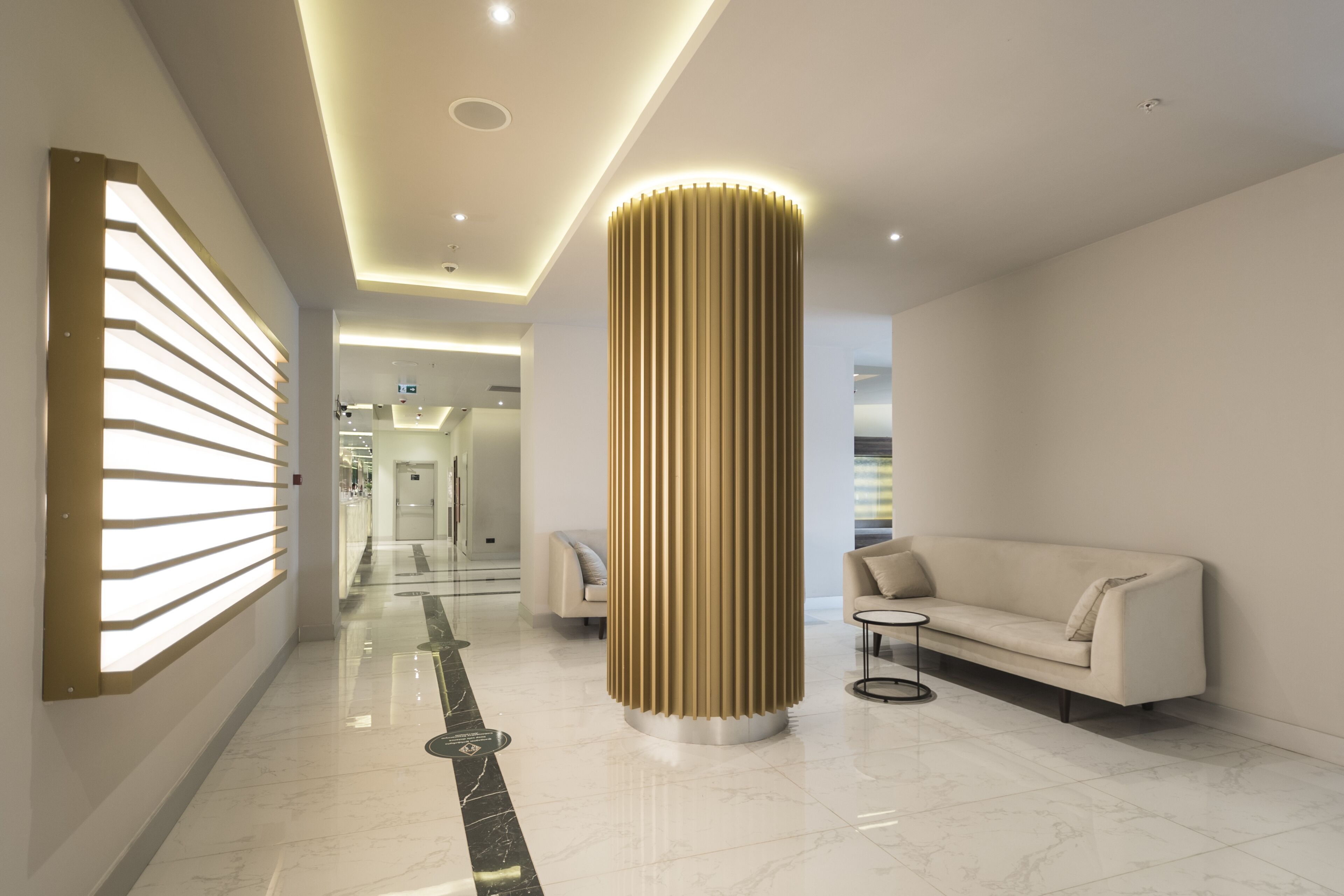 A modern hotel lobby with a central column, a sofa, and a glass partition.