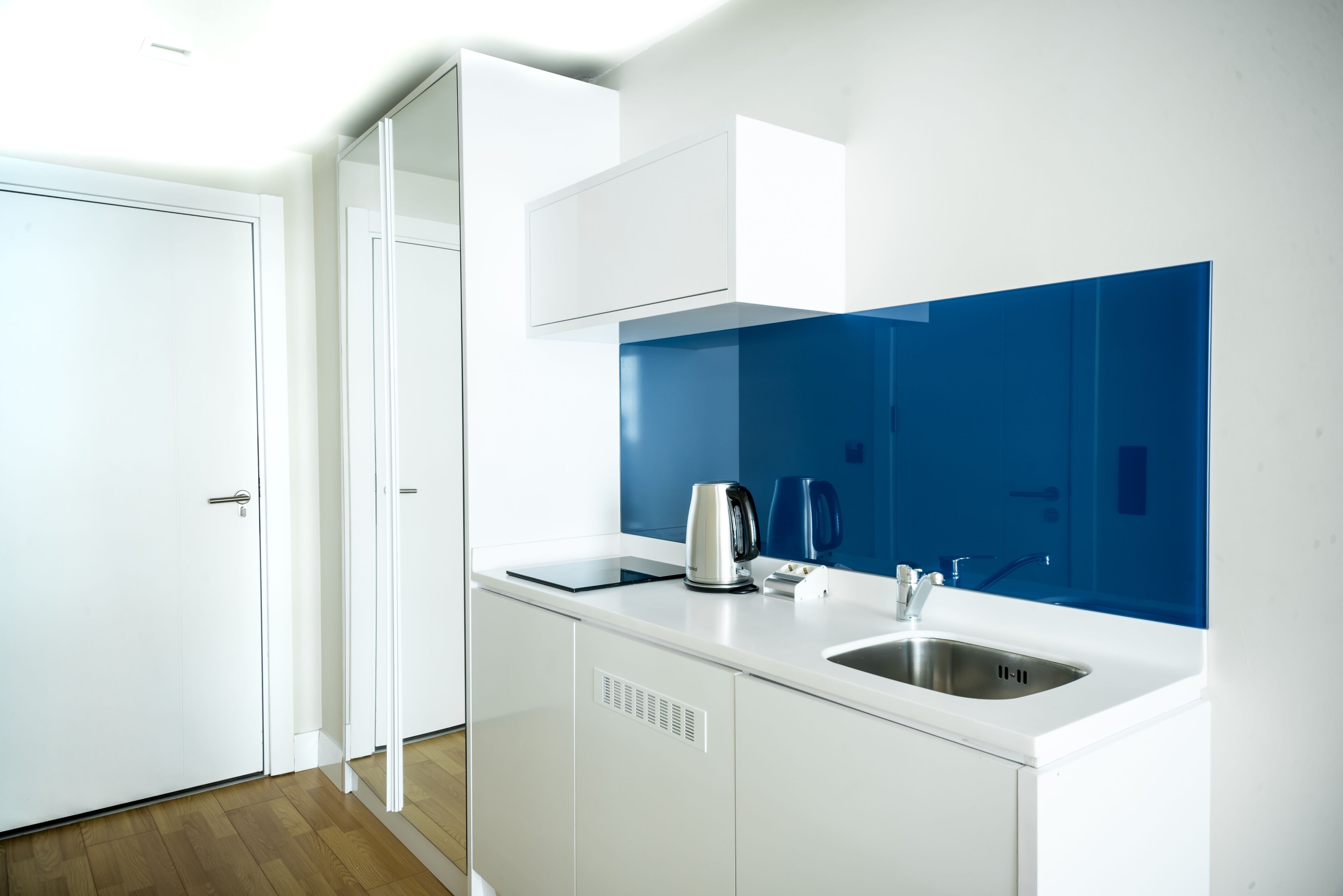 A modern kitchen with white cabinets, a stainless steel sink, and a blue backsplash.