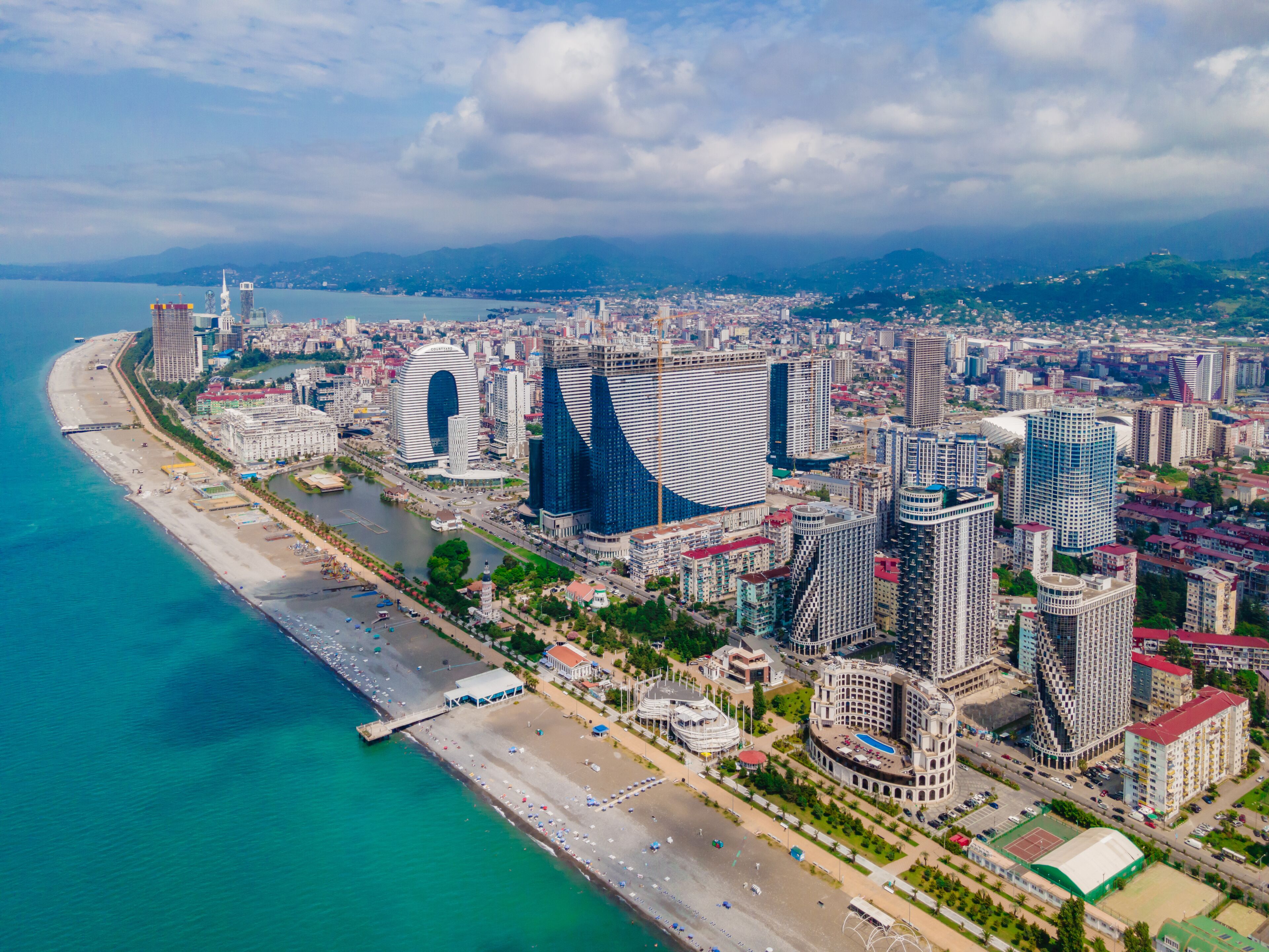An aerial view of a coastal city with modern architecture, including distinctive buildings with unique designs, a marina, and a beach.