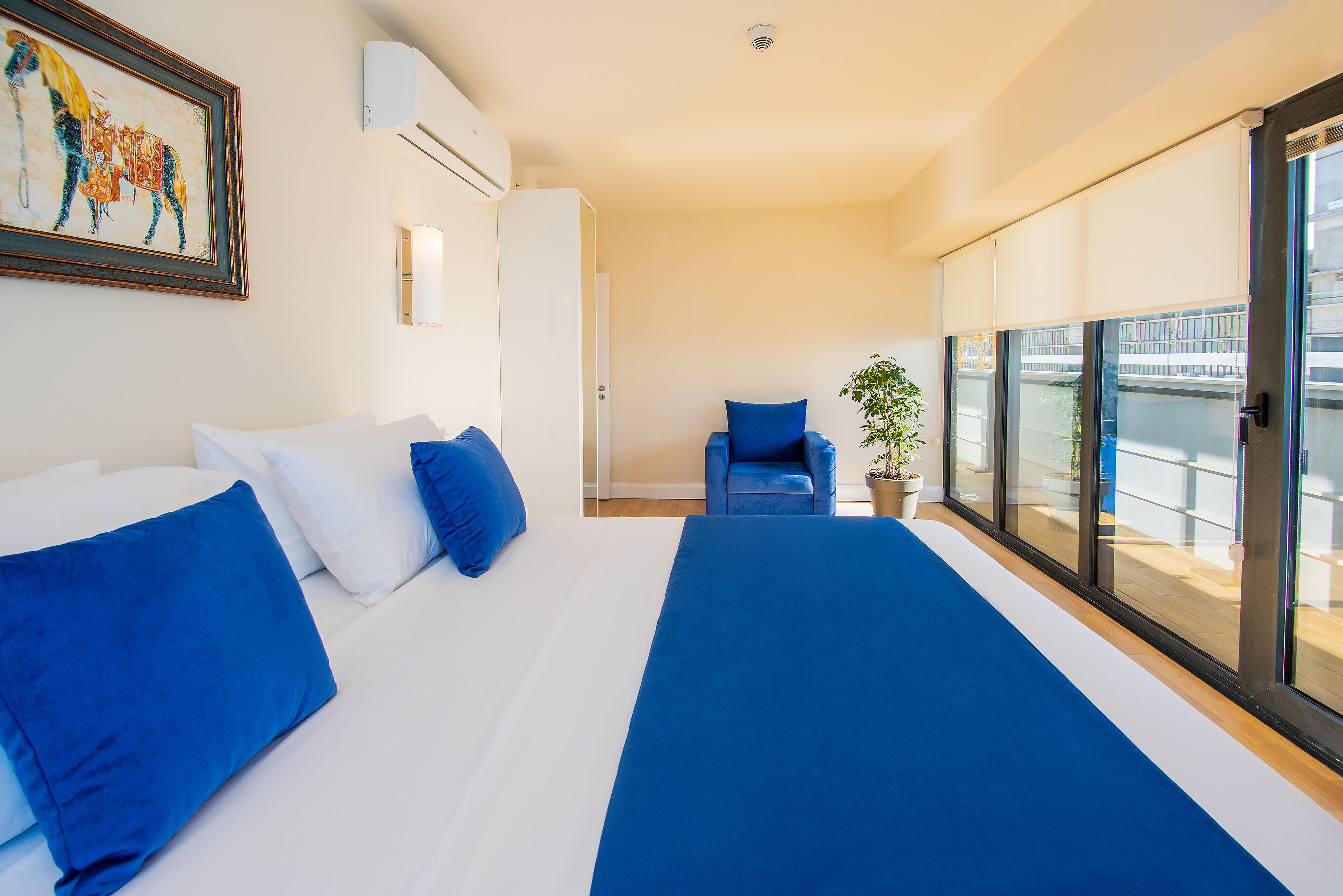 Habitación de hotel con una cama grande, una silla, una planta en maceta y un balcón con vistas.