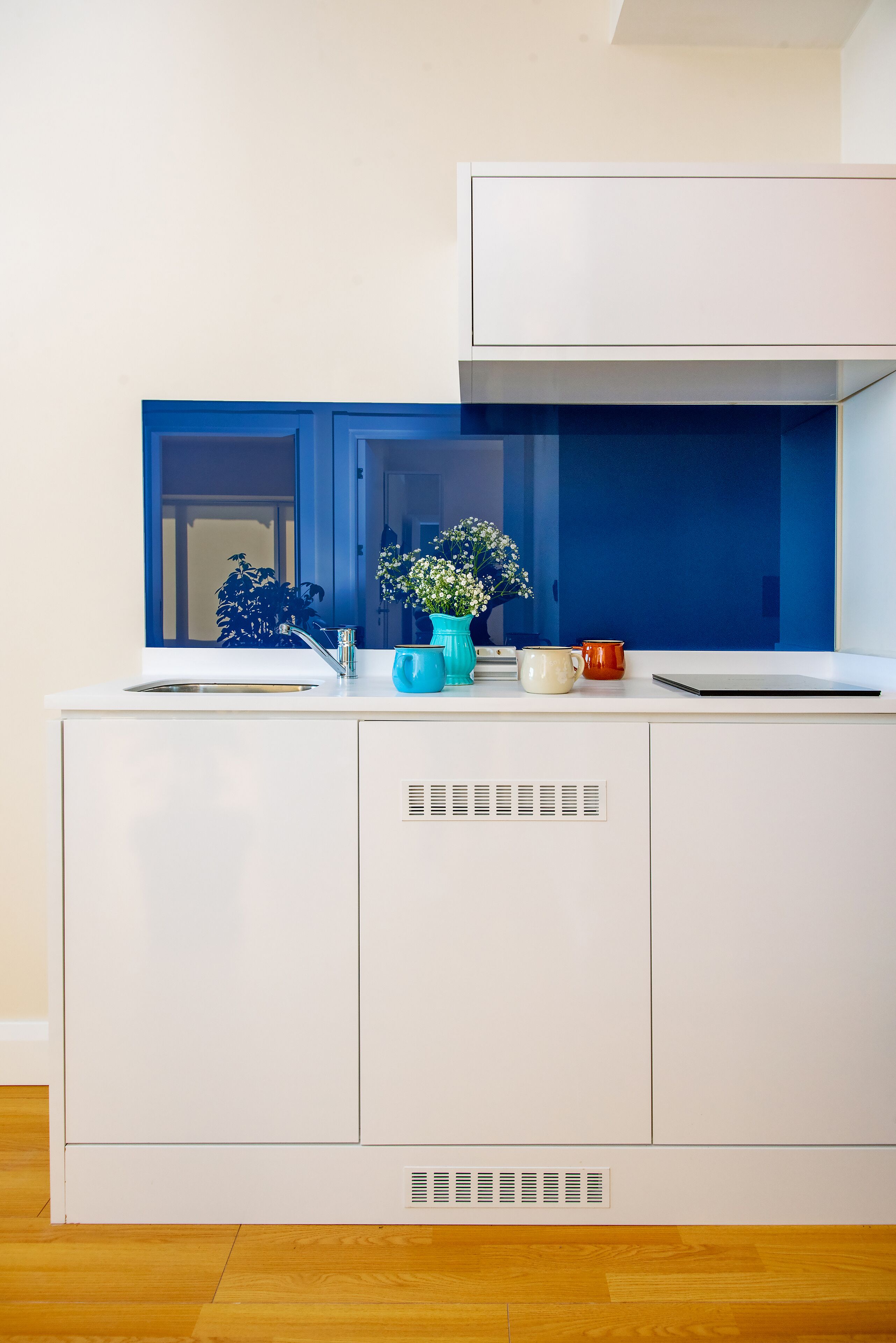 A white kitchen with a blue backsplash, a sink, and a window.