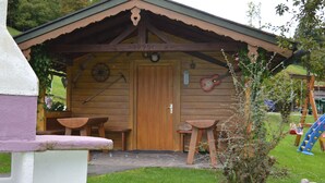A rustic wooden cabin with a wooden door, two wooden benches, and a small table. - Ferienwohnung Watzmann, für 4 Personen (Berchtesgaden)
