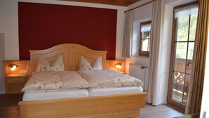 A bedroom with a wooden bed, two bedside tables with lamps, a window with curtains, and a view of greenery outside. - Ferienwohnung Watzmann, für 4 Personen (Berchtesgaden)