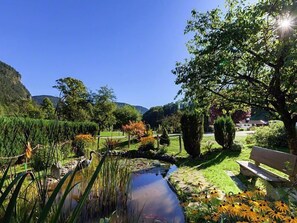 A serene garden with a pond, benches, and a variety of plants and trees.