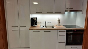 Ett modernt kök med vita skåp, en bänkskiva i trä, en kaffebryggare, en diskho, en rulle hushållspapper och en ugn.