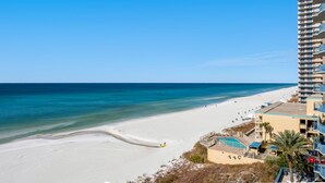 En strand med en klarblå himmel, en sandstrand och en hög byggnad med balkonger som vetter mot stranden.
