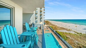 A balcony with blue Adirondack chairs, a pool, and a view of the beach and ocean.