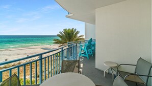 A balcony with a view of the beach and ocean, featuring turquoise chairs and a table.