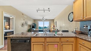 A modern kitchen with granite countertops, stainless steel appliances, wooden cabinets, and a large window offering a view.