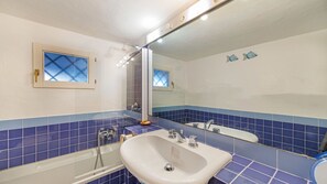 A bathroom with a white sink, blue-tiled walls, a large mirror, and a shower area.