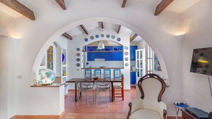 An arched doorway leading to a dining area with a table and chairs, a kitchen with blue cabinets, and a television mounted on the wall. - Casa di Nonna Anna (Olbia)
