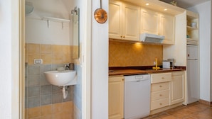 Une cuisine avec des meubles blancs, un évier, un lave-vaisselle et une horloge au mur.