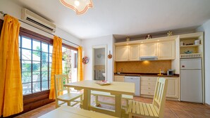 Une cuisine avec une table et des chaises, une fenêtre avec des rideaux et un sol carrelé.