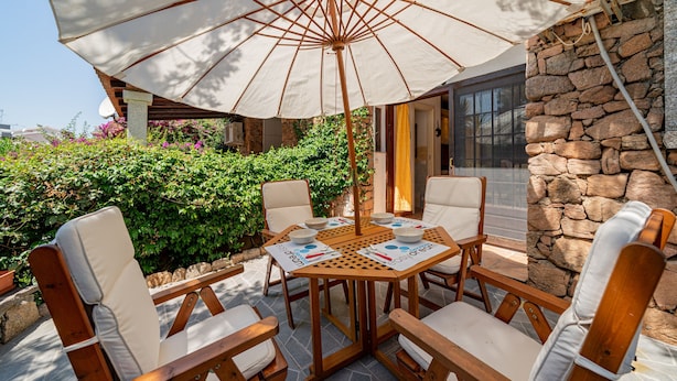 Un espace extérieur aménagé avec une table et des chaises sous un grand parasol, entouré de murs en pierre et de verdure.