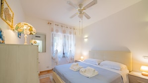 Une chambre à coucher avec un lit, des tables de chevet, un ventilateur de plafond et une fenêtre avec des rideaux.