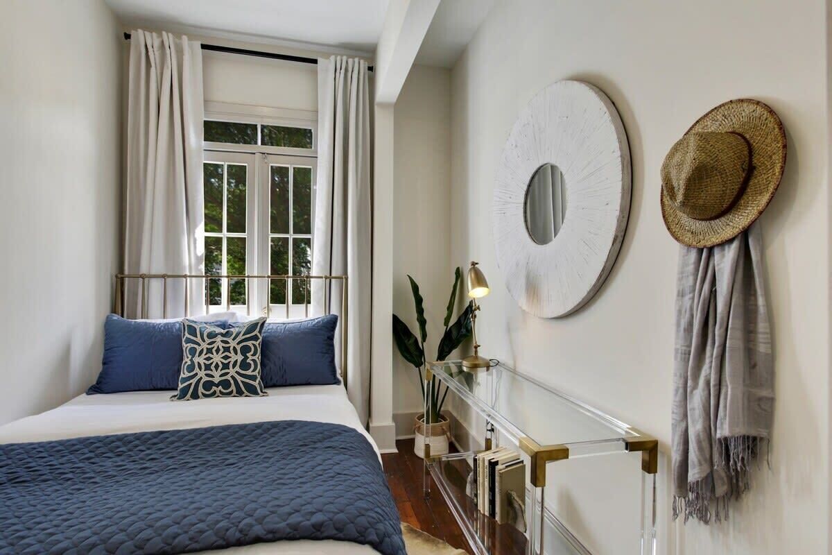 A bedroom with a bed, curtains, a round mirror, a hat, and a plant.