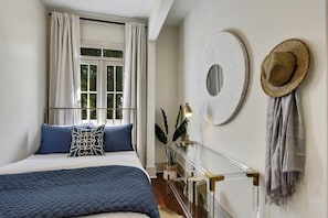 Une chambre à coucher avec un lit, des rideaux, un miroir rond, un chapeau et une plante.