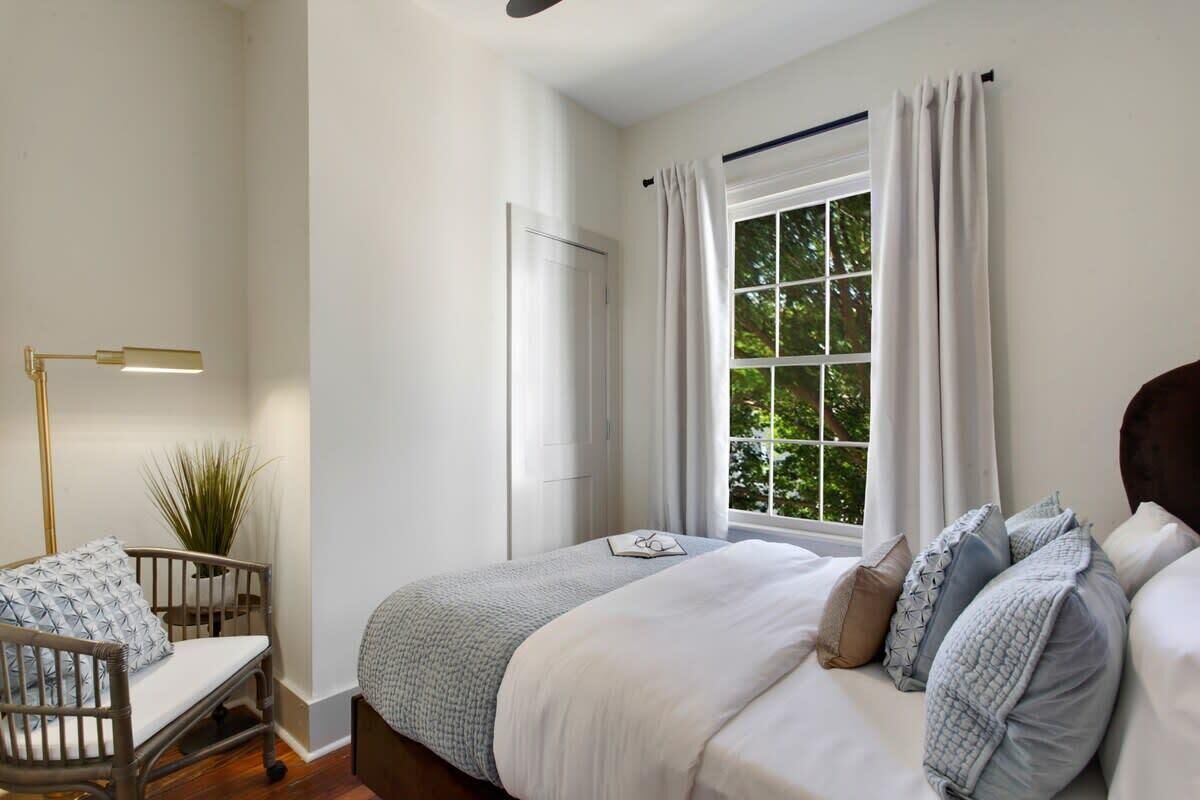 A bedroom with a bed, a desk, a chair, a floor lamp, and a window with curtains.