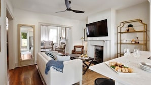 A modern living room with a fireplace, a dining area with a table set for two, and a television mounted on the wall.