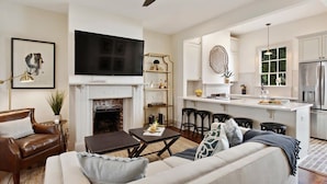 A modern living room with a fireplace, a television, and a kitchen area with bar stools.
