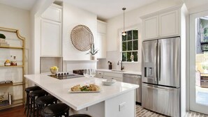 A modern kitchen with white cabinetry, a large stainless steel refrigerator, and a central island with stools.