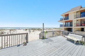 A beachside balcony with a wooden deck, a bench, and a view of the beach and ocean.