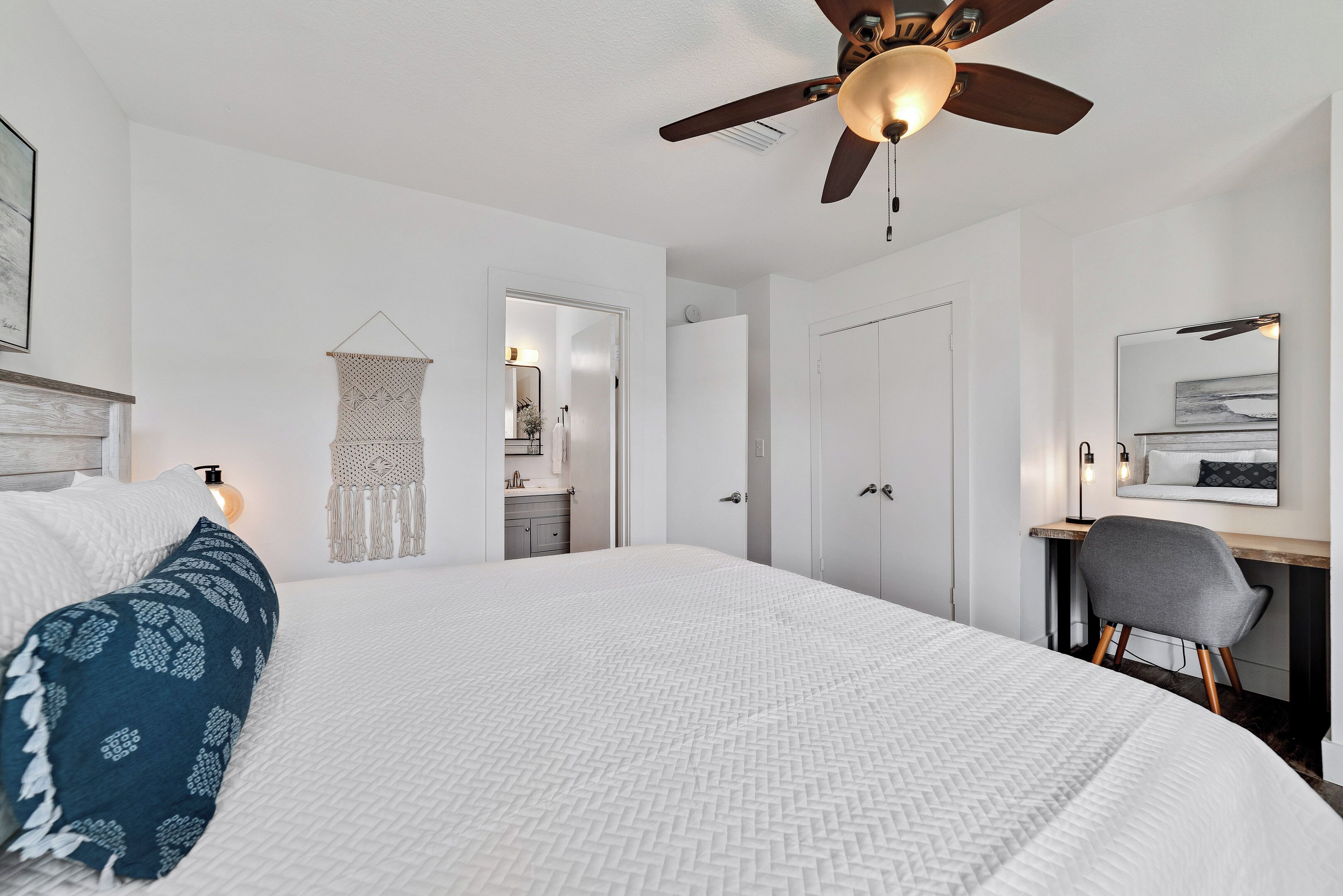 Une chambre avec un grand lit, un ventilateur de plafond, un bureau avec une chaise et une armoire.