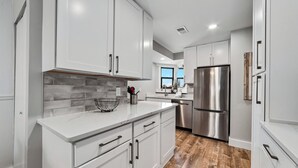 Una cocina moderna con armarios blancos, un refrigerador de acero inoxidable y piso de madera.