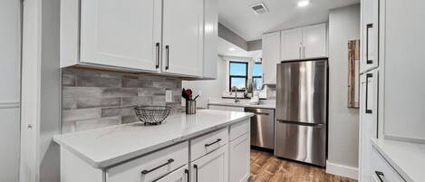 Una cocina moderna con armarios blancos, un refrigerador de acero inoxidable y piso de madera.