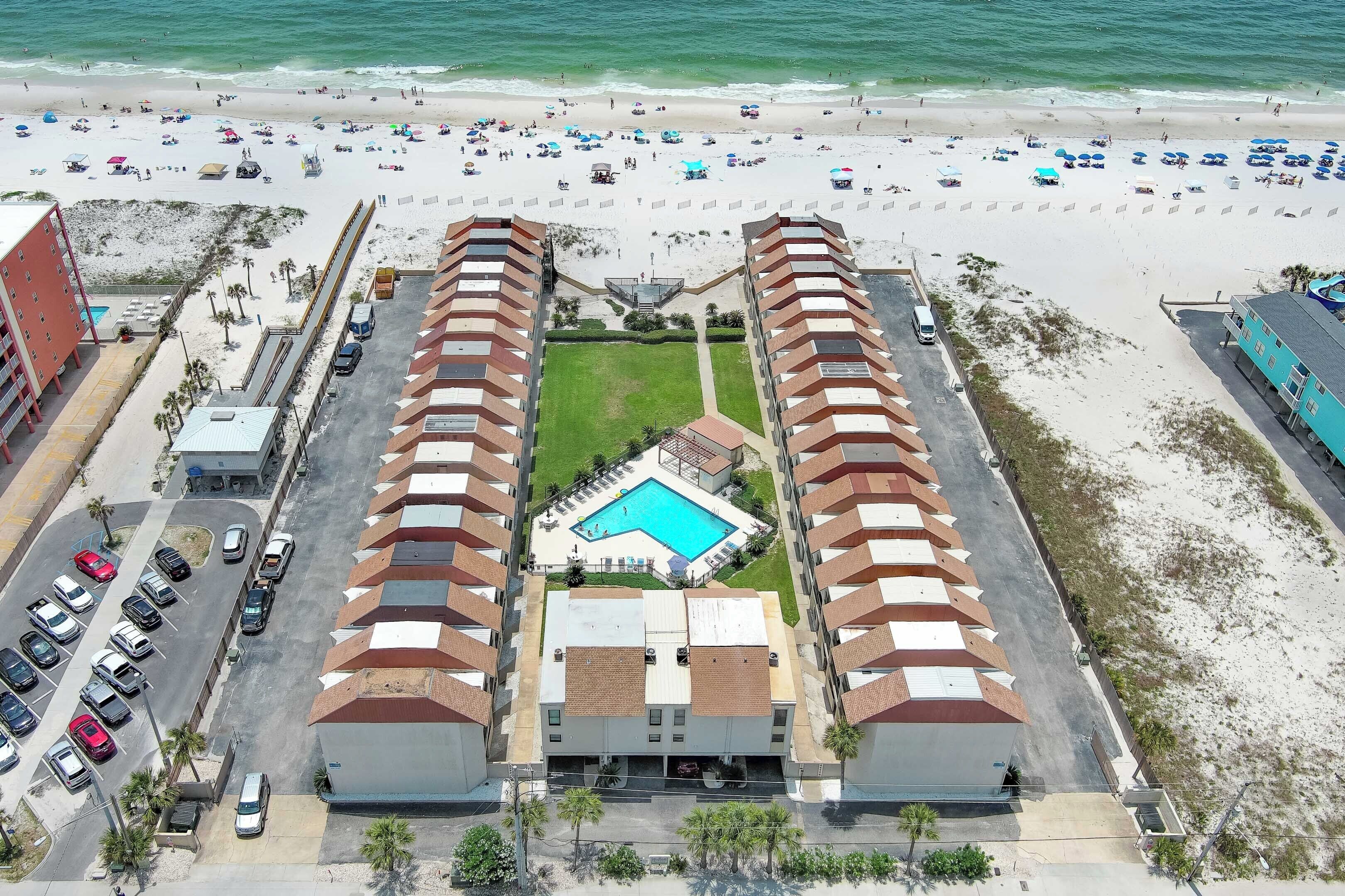 A hotel with a swimming pool, parking lot, and beach view.