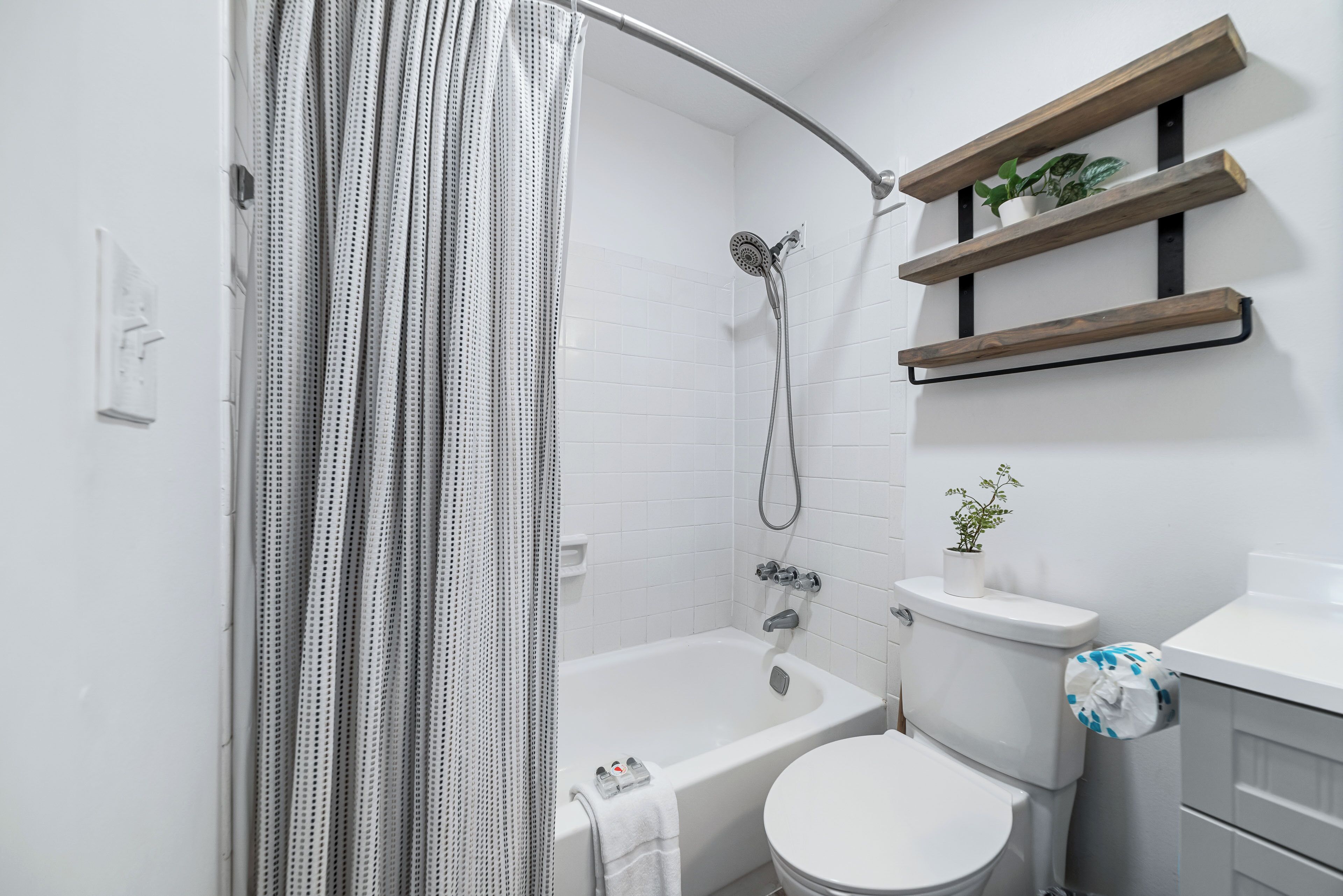 A modern bathroom with a shower, toilet, and built-in shelves with plants.