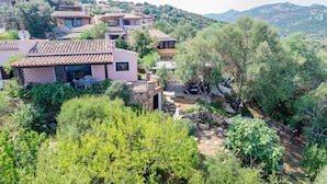 A hillside property with multiple buildings, including a pink house with a patio and stone walls. - Casa Girgolu (Loiri Porto San Paolo)