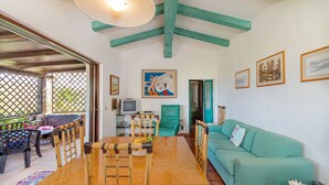 A cozy living room with a wooden dining table, green sofa, and a TV. - Casa Girgolu (Loiri Porto San Paolo)