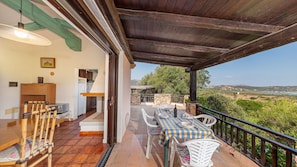 A covered outdoor dining area with a table set for two, a wooden chair, and a view of the countryside. - Casa Girgolu (Loiri Porto San Paolo)