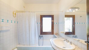 A bathroom with a bathtub, a sink, a shower, and a window. - Casa Girgolu (Loiri Porto San Paolo)