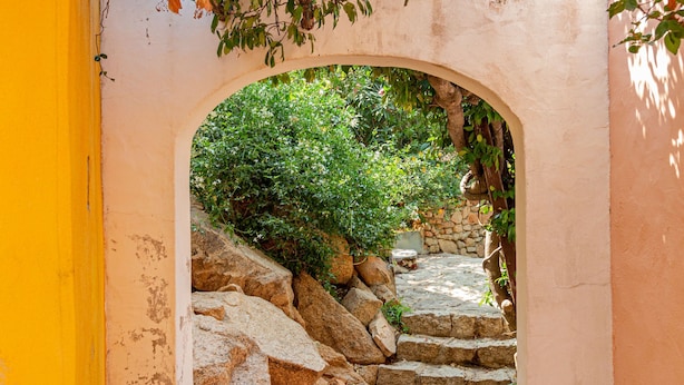 A stone staircase leading to a covered area with a view of greenery and a stone wall. - Casa Girgolu (Loiri Porto San Paolo)