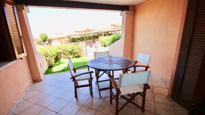Un balcó amb una taula rodona i cadires, vista a un jardí, i un edifici al fons.