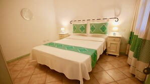 A bedroom with a bed, two bedside tables, a nightstand, a lamp, a wall clock, and a curtain. - Casa Susy (Loiri Porto San Paolo)