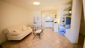 A compact living space with a sofa, a small dining table, and a kitchenette. - Casa Susy (Loiri Porto San Paolo)
