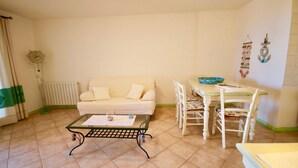 A living room with a sofa, a glass coffee table, a dining table with chairs, and a wall clock. - Casa Susy (Loiri Porto San Paolo)